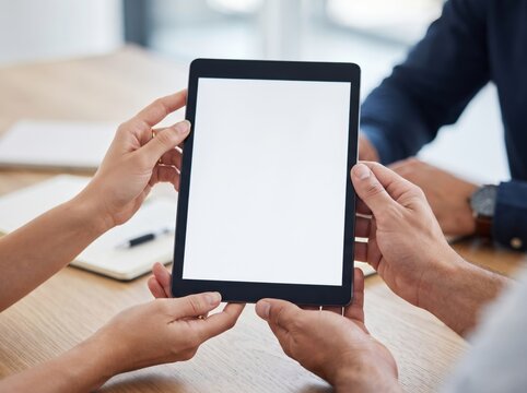 Close-up of colleagues holding a digital tablet with a blank white screen mockup during a team meeting in a modern office, offering copy space for app or website display.