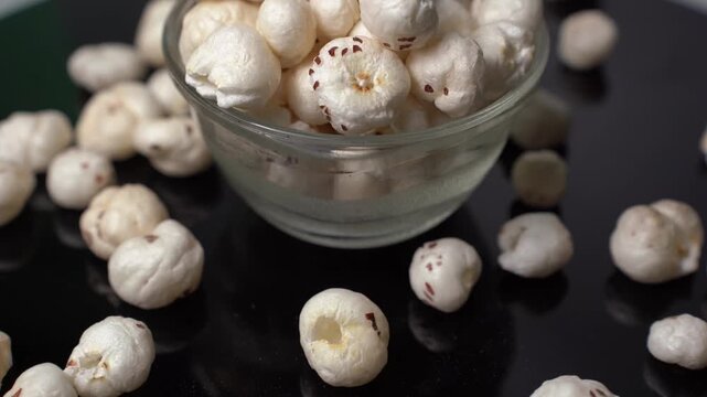 Fox nut, Euryale ferox, puffed lotus seed snack in glass bowl on dark surface, healthy organic vegetarian food product concept