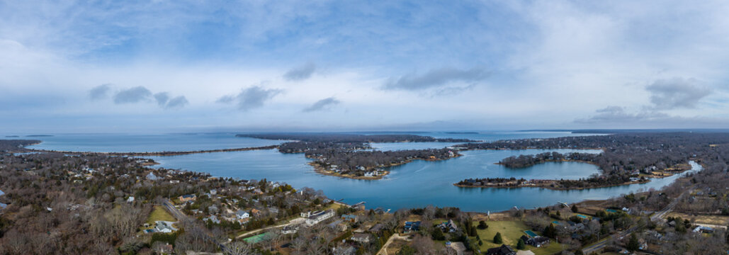 Aerial view of Sag Harbor Cove surrounded by residential properties, bare trees, and calm waters under a cloudy sky in Sag Harbor, NY, United States.