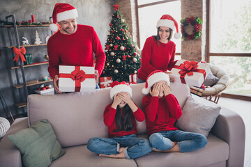 Naklejka premium Family celebrating Christmas at home with parents surprising children with wrapped gifts by a decorated tree