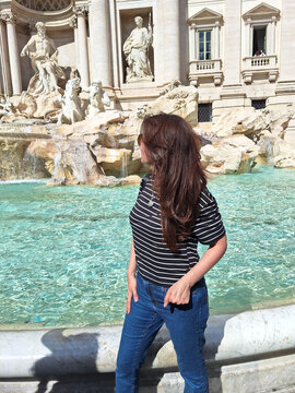 Mujer turista de cabello casta&ntilde;o admirando la hist&oacute;rica Fontana di Trevi en Roma, Italia, durante un soleado d&iacute;a de verano