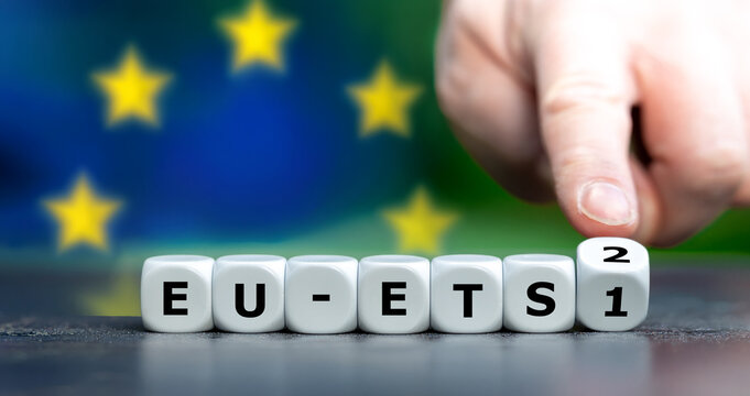 Finger dreht einen Zahlenw&uuml;rfel von EU-ETS 1 auf EU-ETS 2 &ndash; Symbol f&uuml;r das neue Emissionshandelssystem f&uuml;r Geb&auml;ude und Stra&szlig;enverkehr.
