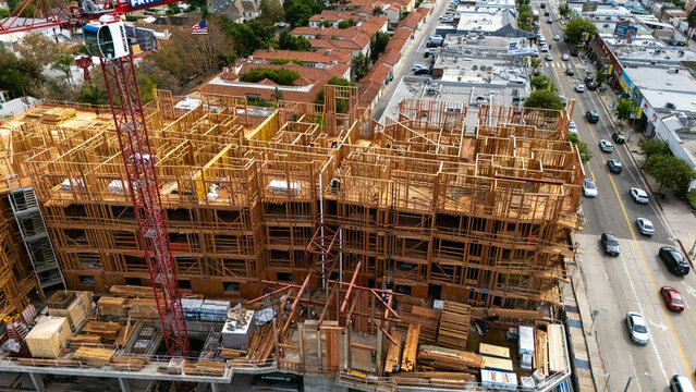 Aerial view of a wooden building construction site with a red tower crane, surrounded by urban streets in Los Angeles, California, United States.