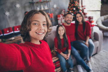 Naklejka premium Happy family Christmas selfie at home with parents and children sitting by decorated Christmas tree and wrapped gifts celebrating holiday together