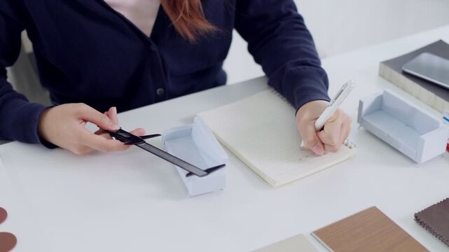 Interior designer measuring miniature sofa model with caliper while writing notes at studio desk