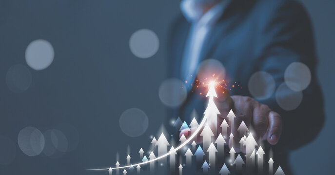 A businessman in a suit gestures toward a soaring cluster of upward-pointing arrows. Multiple ascending arrows signify a collective market surge, strong economic progress, and high performance.