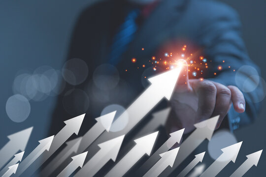 A business professional in a dark suit touches the peak of a prominent upward-pointing arrow. Multiple ascending arrows signify a collective surge in market momentum and shared economic success.