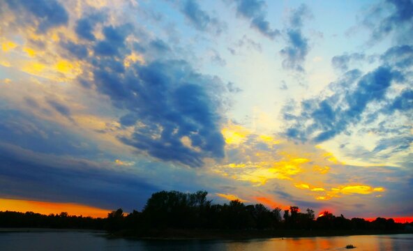 Colorful sunset above the peaceful lake with dramatic burning clouds and trees silhouettes, peaceful lake sunset landscape