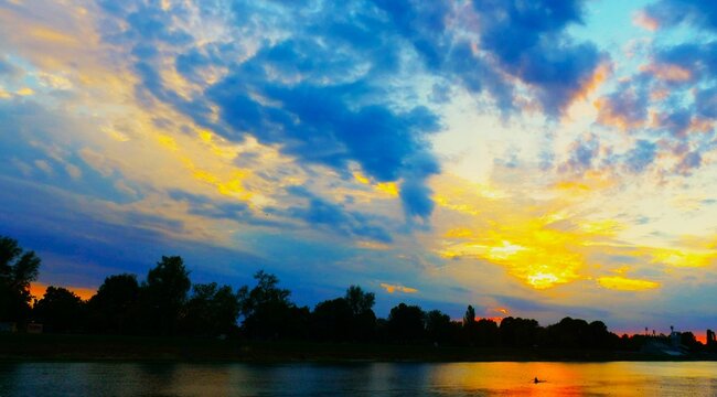 Colorful sunset above the peaceful lake with dramatic burning clouds and trees silhouettes, peaceful lake sunset landscape