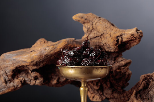 Spicy dried black olives in a vintage brass bowl on a background of weathered olive tree snags.