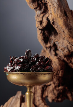 Spicy dried black olives in a vintage brass bowl on a background of weathered olive tree snags.