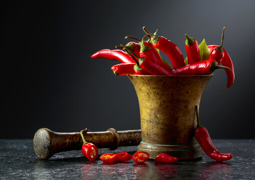 Fresh red chili peppers in old brass mortar on a black table.