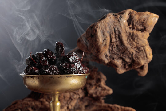 Dry cured black olives in a vintage brass bowl on a background of weathered olive tree snags.