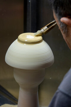 Close-up of a mushroom shaped porcelain bowl spinning on a wheel being finished with a brush along its rim, Kyushu region, Arita, Japan