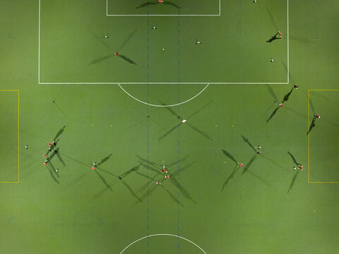 Aerial view of a floodlit soccer field with players during a nighttime football match or training session, featuring long shadows cast on the green pitch in Krakow, Lesser Poland Voivode, Poland.