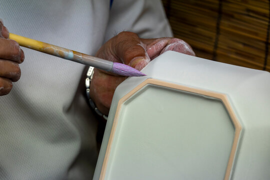 Artisan's hand painting purple glaze along the edge of an octagonal white bisque porcelain lid, Kyushu region, Arita, Japan
