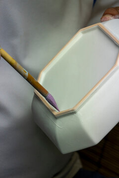 Artisan's hand painting purple glaze along the interior edge of a hexagonal white bisque porcelain box, Kyushu region, Arita, Japan