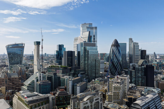 Aerial view of the London skyline featuring iconic skyscrapers including 30 St Mary Axe and 22 Bishopsgate under a clear blue sky in the United Kingdom.
