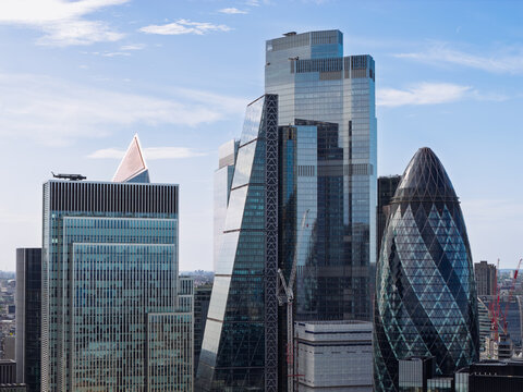 Aerial view of the City of London skyline featuring The Gherkin, The Leadenhall Building, and 22 Bishopsgate under a blue sky, United Kingdom.