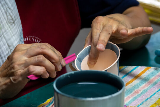 Close-up of an artisan's hands dipping a porcelain cup into pink glaze, Kyushu region, Arita, Japan