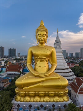 Aerial view of the giant golden Buddha statue at Wat Paknam Phasi Charoen, surrounded by urban rooftops and a white stupa in Bangkok, Krung Thep Maha Nakho, Thailand.