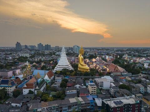 Aerial view of Wat Paknam Phasi Charoen featuring the giant golden Buddha statue and white stupa amidst the dense urban landscape of Bangkok, Krung Thep Maha Nakhon, Thailand.