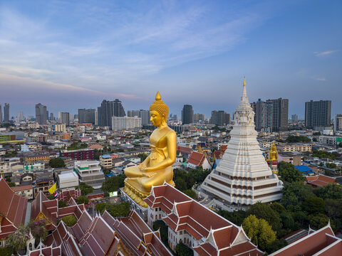 Aerial view of the giant golden Buddha statue and the white stupa at Wat Paknam Phasi Charoen surrounded by the urban skyline of Bangkok, Krung Thep Maha Nakhon, Thailand.
