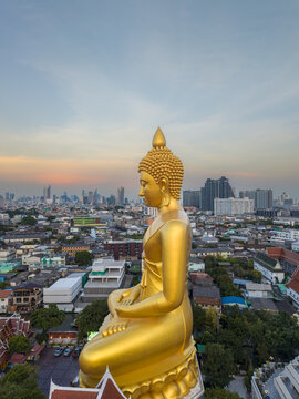 Aerial view of the giant golden Buddha statue at Wat Paknam Phasi Charoen overlooking the dense urban landscape during the golden hour in Bangkok, Krung Thep Maha Nakhon, Thailand.