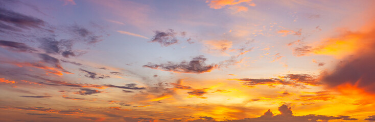 Fototapeta premium Panoramic Dramatic Sunset Sky with Colorful Orange and Purple Clouds,A wide panoramic shot of a dramatic sky during sunset, showcasing vibrant gradients of warm yellow, bright orange, and soft purple 