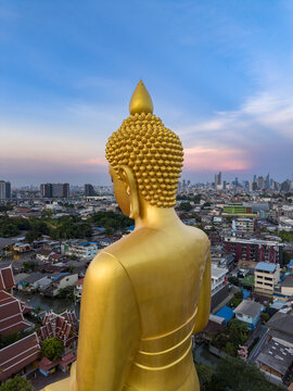 Aerial view of the golden Buddha statue at Wat Paknam Phasi Charoen overlooking the dense urban landscape and rooftops of Bangkok at sunset. Bangkok, Krung Thep Maha Nakho, Thailand.
