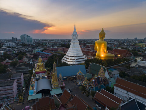 Aerial view of Wat Paknam Phasi Charoen featuring the massive golden Buddha statue and white stupa at sunset in Bangkok, Krung Thep Maha Nakhon, Thailand.