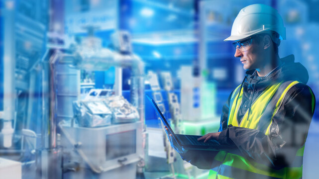 Industrial manufacturing, engineer monitors automated production equipment with a laptop for process control, diagnostics and factory maintenance.