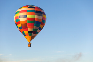 Obraz premium Colorful hot air balloon drifts across an open blue sky with extensive copy space. Concept of peaceful flight, freedom, exploration, balloon tourism and adventure travel.