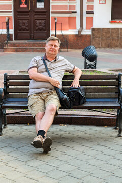 mature blond man sits happily on park bench enjoying rest and fresh air during the day.