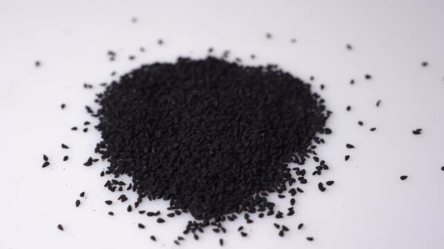 Nigella sativa, black cumin seeds, kalonji, or black caraway pile on white surface, studio shot closeup, macro ingredient clip