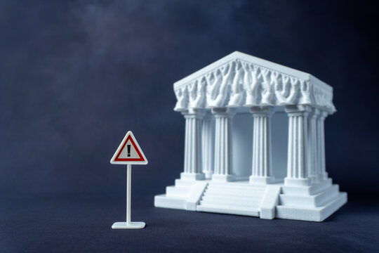 Warning sign and a blurred white classical courthouse model. Legal hazards, judicial risk, regulatory compliance warnings, or constitutional crisis concept.
