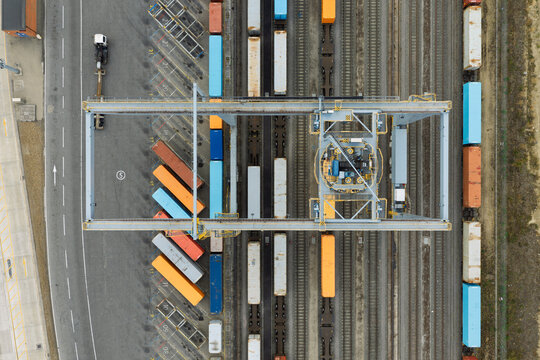 Aerial view of a busy rail freight terminal with colorful shipping containers loaded onto trains and a large gantry crane operating over the tracks in the United Kingdom.