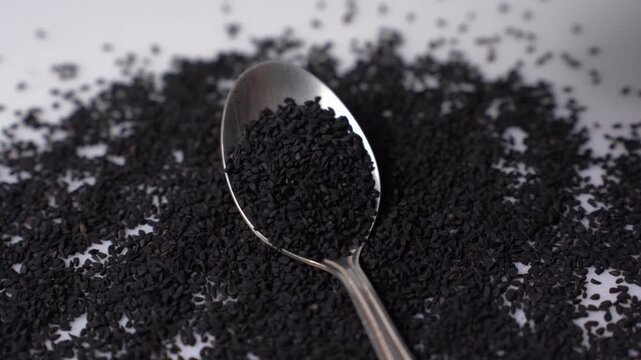 Nigella sativa black cumin seed on metal spoon macro close up studio shot on white background for health, spice, and herbal remedy
