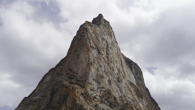 Rugged mountain peak The Gumbok Rangjon under cloudy sky with golden hues in Zanskar Valley of Ladakh, India. dramatic rock formation against overcast backdrop; serene and majestic