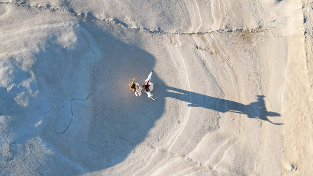 Aerial view of two people walking on the white volcanic rock formations of Sarakiniko beach with long shadows cast on the textured surface in Milos, Greece.
