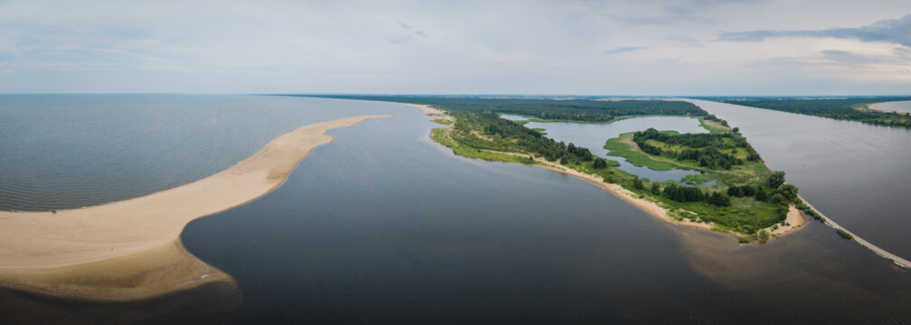 Aerial view of the Vistula River mouth meeting the Baltic Sea, featuring a sandy spit, lush wetlands, and calm water under a cloudy sky in Mikoszewo, Pomeranian Voivodeship, Poland.