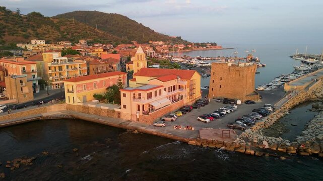 Acciaroli Cilento drone sunset flight church watchtower courtyard marina reveal, low camera angle over coastal complex, Italian seaside village harbor cinematic footage 4k