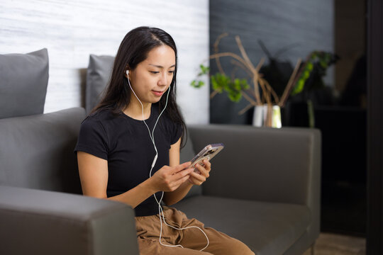 Woman sitting on couch listening to music with earphones