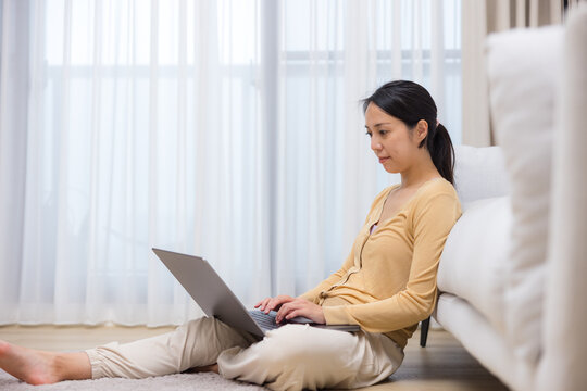 Woman typing on laptop sitting on floor at home