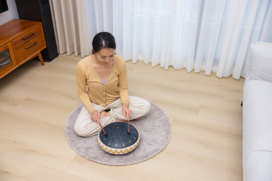 Woman sitting on rug playing singing drum in room