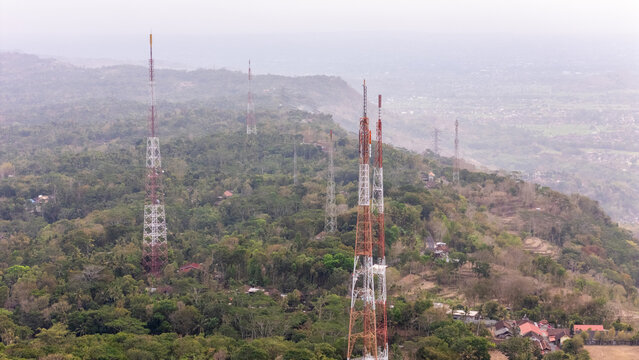 Aerial view of telecommunication towers rising above the dense forest and hilly landscape of Nglanggeran in Patuk, Special Region of Yogyakarta, Indonesia.