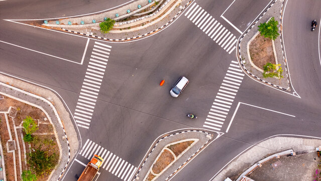 Aerial view of a road intersection with a car, a motorcycle, and a truck, with crosswalks and surrounding vegetation in Patuk, Special Region of Yogyakarta, Indonesia.