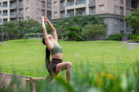 Woman doing kneeling lunge yoga pose on lawn outdoors