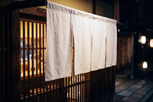 夜の和食店の入口に掛かる白い暖簾と温かな灯り