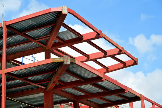 red painted steel structural frame of office building with bare beams, columns, posts and galvanized meal deck slab. closed section beams. welded connections.  low angle view. blue sky background.  